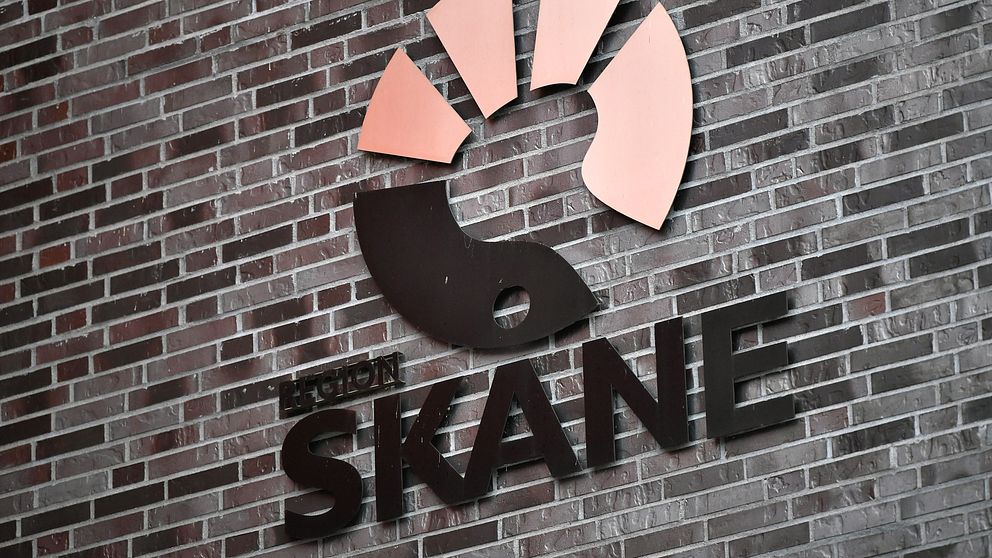 Logotypen för Region Skåne, med en stiliserad hand och solstrålar i orange och svart, placerad på en tegelvägg.
