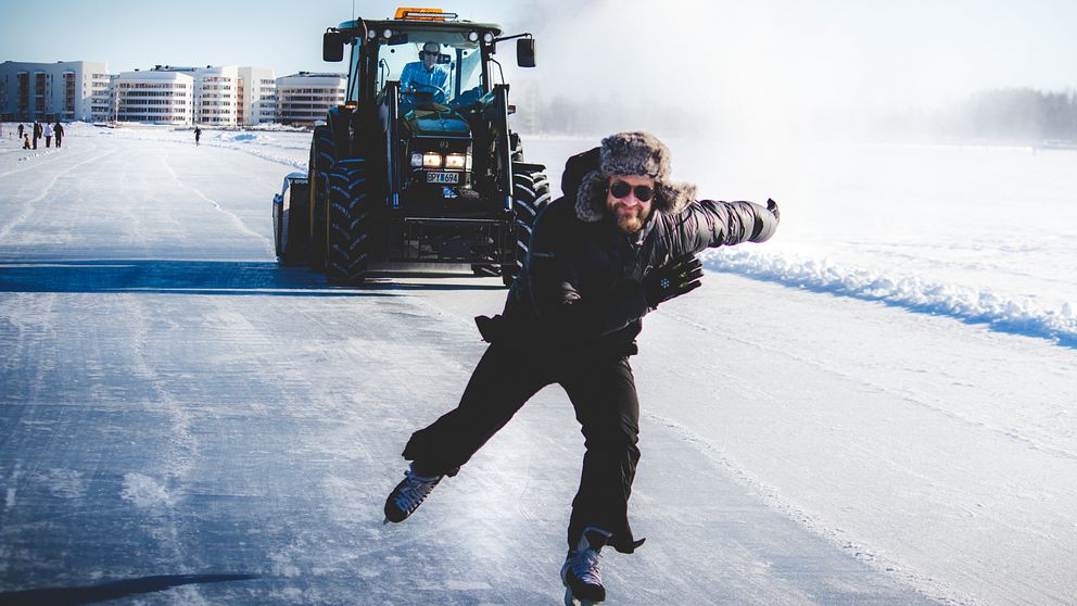 En skridskoåkare i full färd med en traktor hack i häl på isbanan nedanför Södra hamn i Luleå.