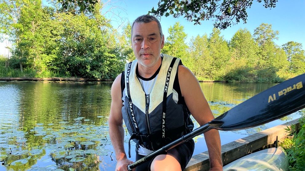 Man sitter vid upp och nedvänd kayak med paddel