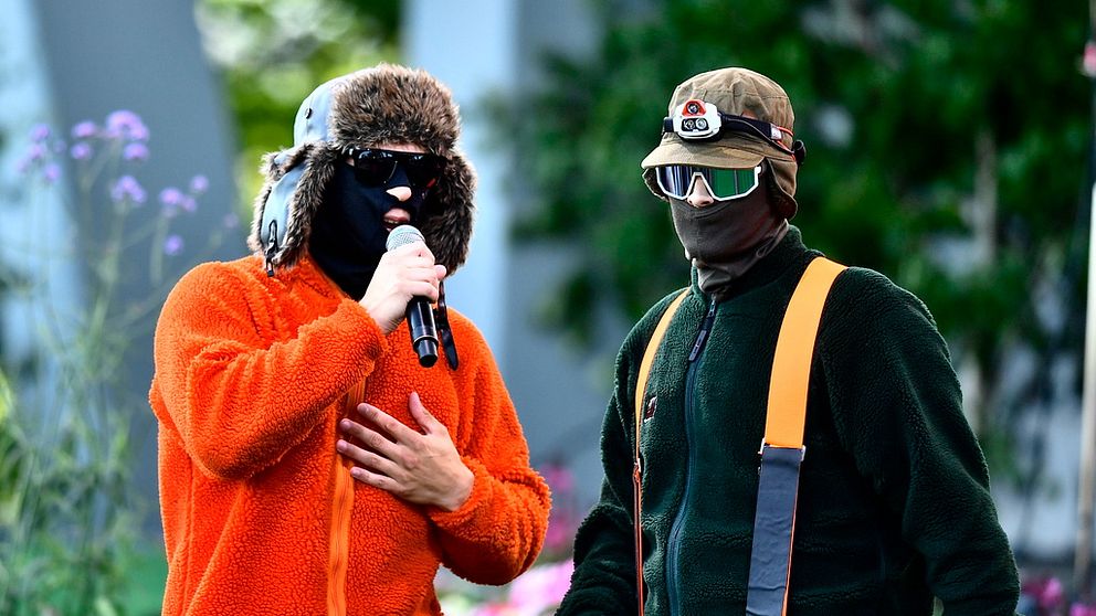 två personer som är maskerade i ansiktet, iklädda skogskläder och mössor samt stora mörka glasögon