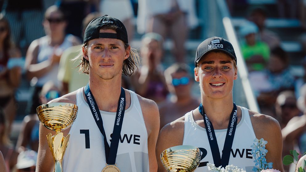 Jacob Hölting Nilsson och Elmer Andersson poserar med pokaler efter beachvolleybollseger.