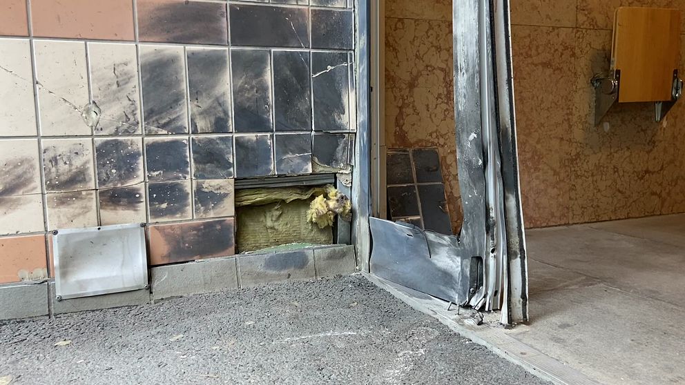 Bild från en av explosionerna vid en entré till ett lägenhetshus. Entrédörren är förstörd och dörrkarmen samt vägg är svarta.