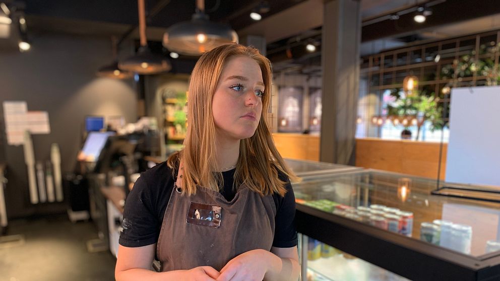 Ung kvinna står i en cafémiljö i Vetlanda. Ser sorgsen ut.