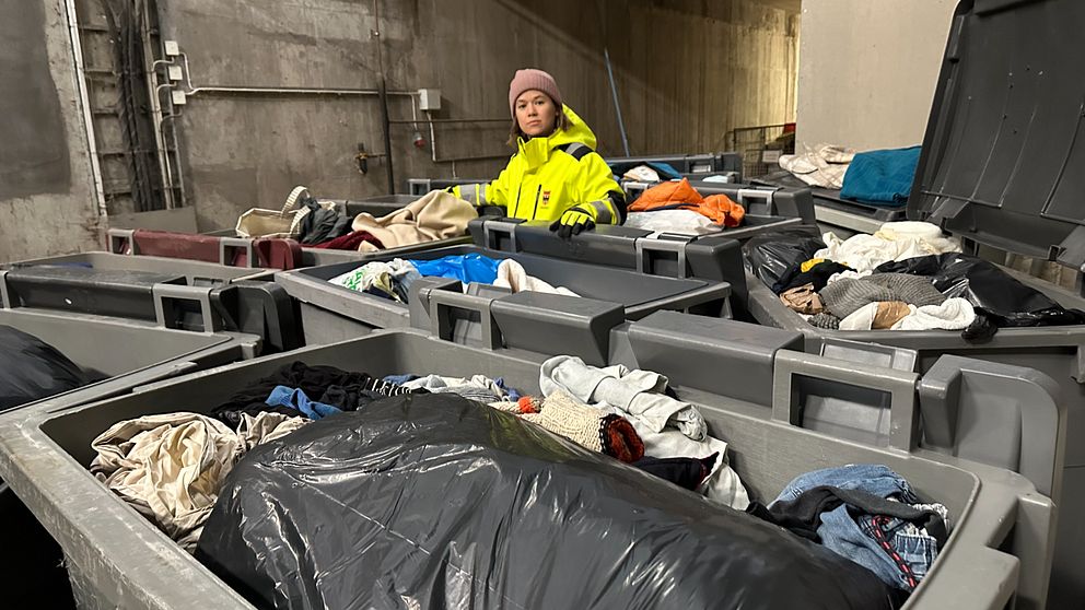 Karolina Werme på Örebro kommuns avfallshantering arbetar bland flera containrar fyllda med begagnade kläder och textilier i en industrimiljö.