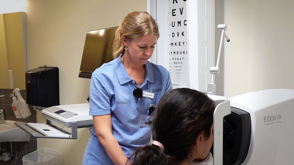 En läkare gör en ögonbottenundersökning. I bakgrunden syns en bokstavstavla.