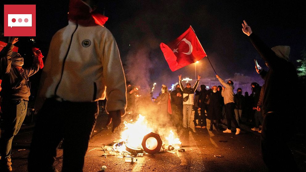 Folkmassa med turkiska flaggor kring eld, nattprotest.