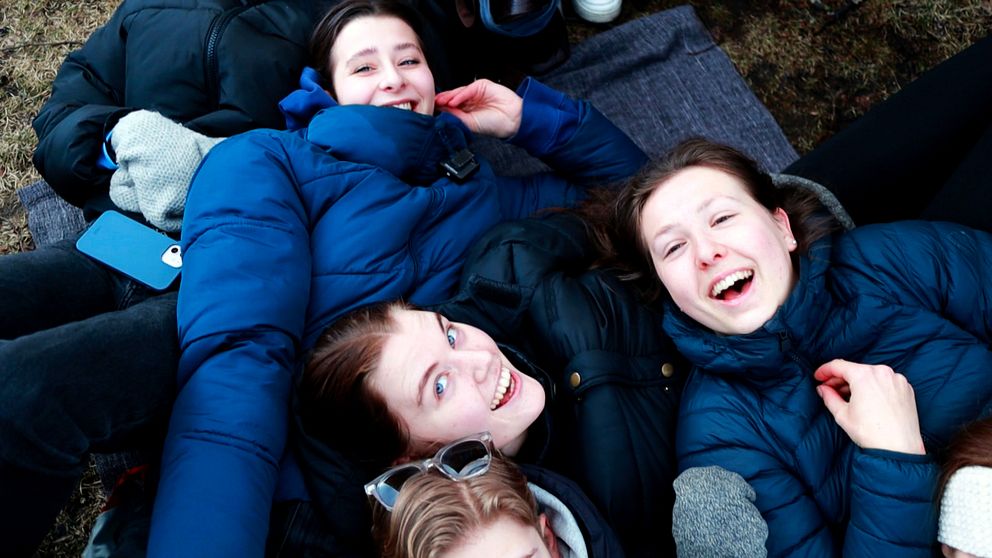 Tre unga tjejer ligger på marken i kön till Östgöta Nations valborgsbiljetter.