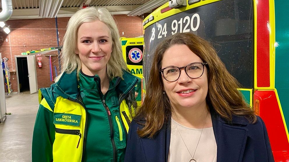 Ambulanssköterskan Greta Berglund står bredvid regionråd Malin Gabrielsson i ambulansgaraget.