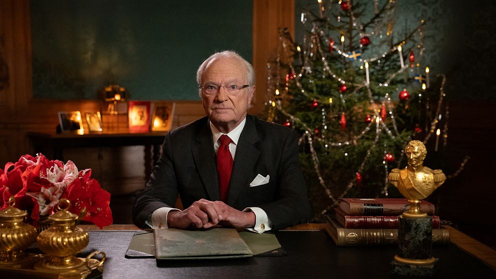 Hans Majestät Konungen sitter vid ett skrivbord omgiven av julpynt och en julgran i bakgrunden.