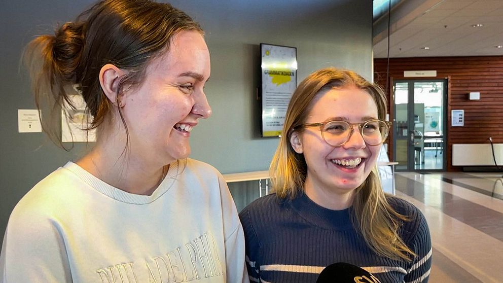 Två tjejer i 20-årsåldern står i en korridor på Karlstads universitet och skrattar.