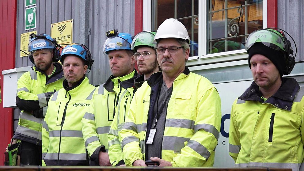 Sex byggarbetare står med sammanbitna miner under den tysta minuten.