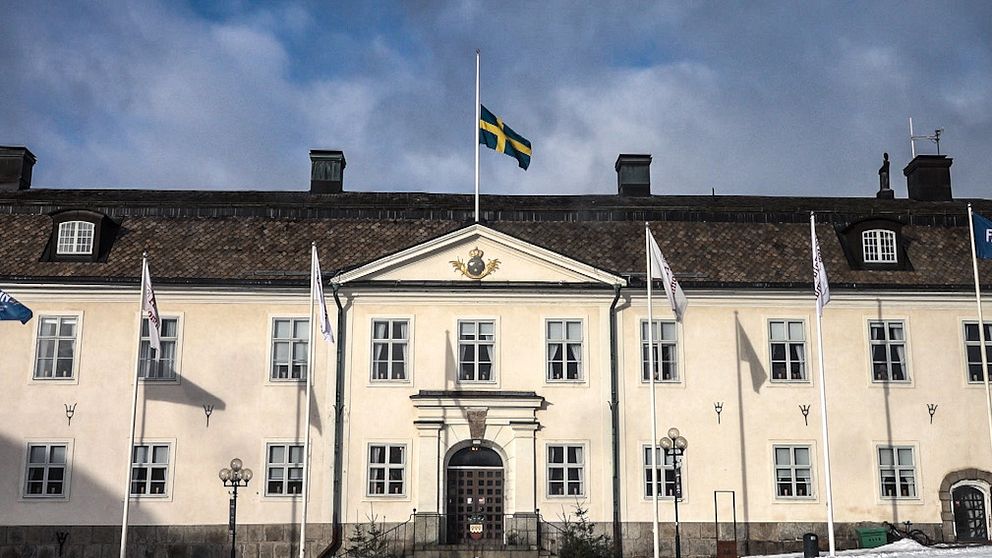 Rådhuset i Falun, med en svensk flagga på halv stång och flera vita flaggor på rad framför entrén. Himlen är molnig.