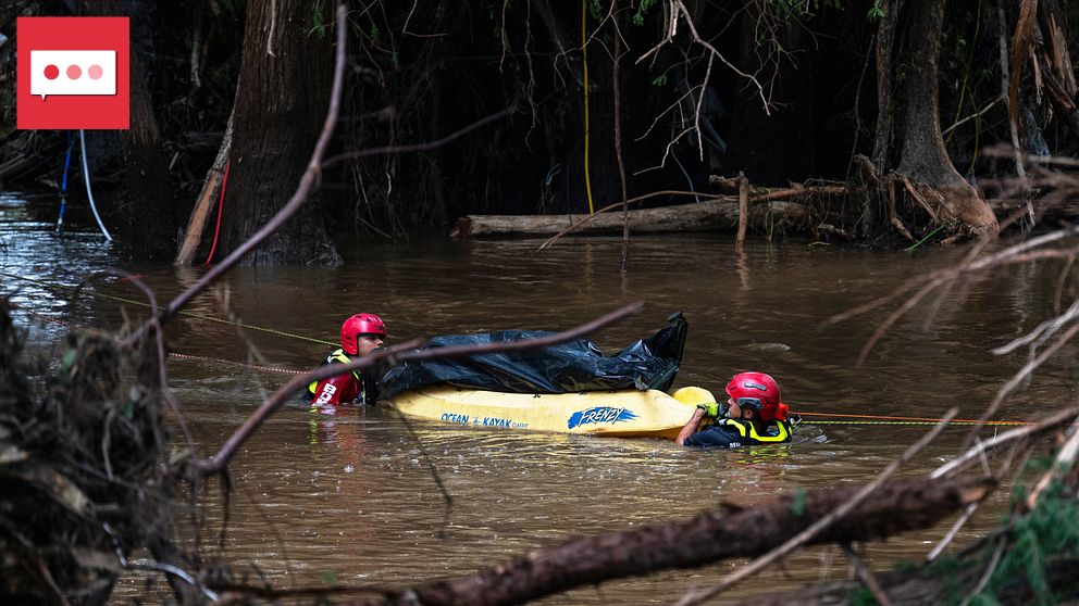 Räddningsarbetare i vatten under översvämning, omgivna av träd och brunt vatten.