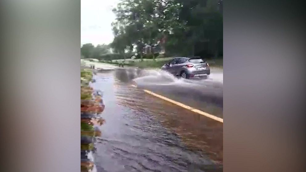Bil kör in i en översvämmad väg.
