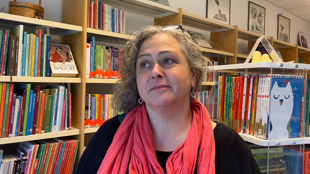 Lotta Lejon Stenberg står framför bokhylla på bibliotek.