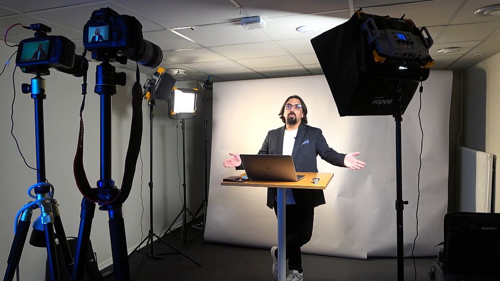 En person håller digital föreläsning framför kamera och strålkastare i studio.