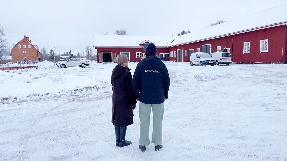 En kvinna med kort grått hår samt en kvinna med gröna byxor står framför församlingens röda, stora lada i Lima.