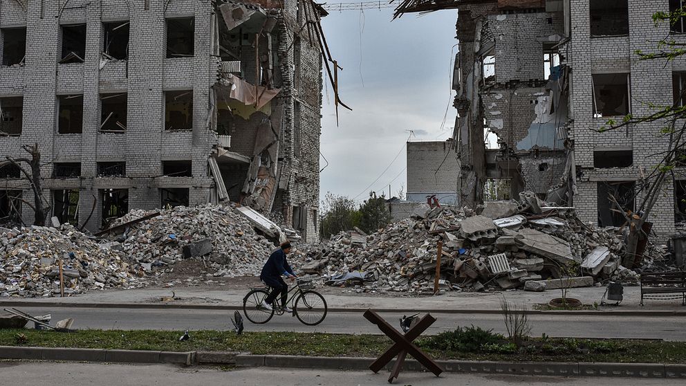 En kvinna cyklar vid en bombad byggnad i Orkihiv, Ukraina.