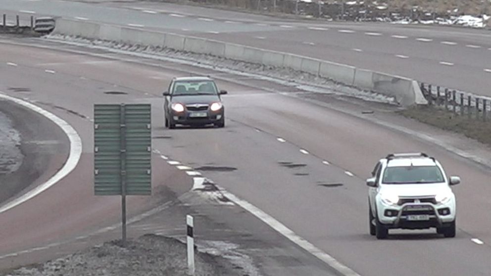 Flera stora potthål och två passerande personbilar syns på motorvägen E20.