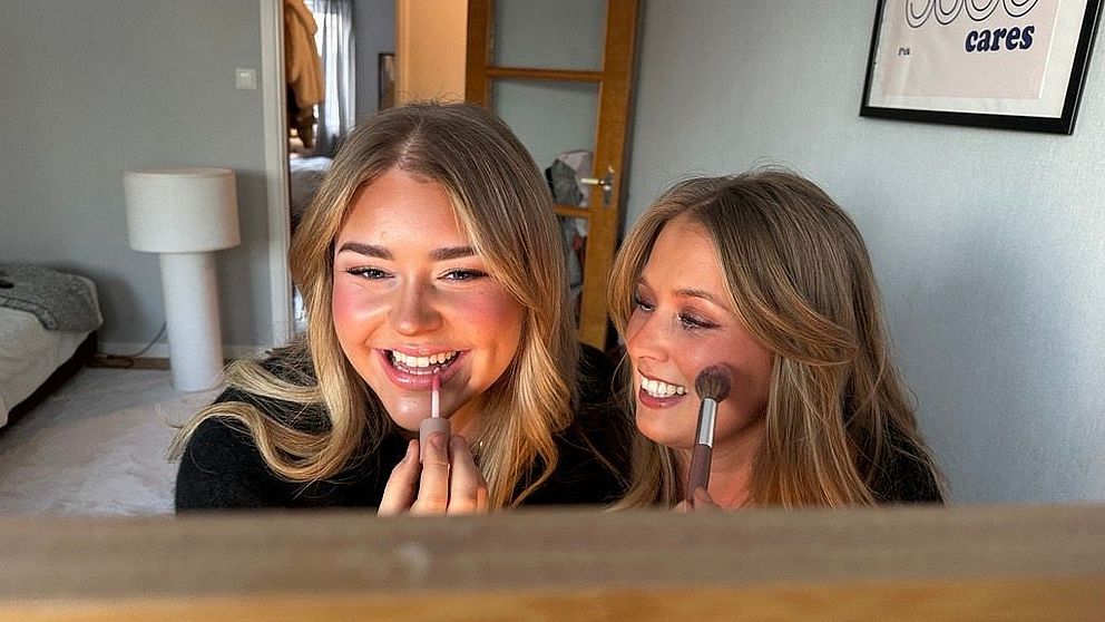 Emma Grönlund och Lovisa Skog sitter framför en spegel i ett sovrum och sminkar sig
