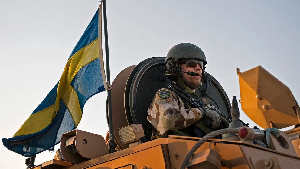 Bild på en svensk soldat med sandfärgad uniform. Svensk flaga bredvid.