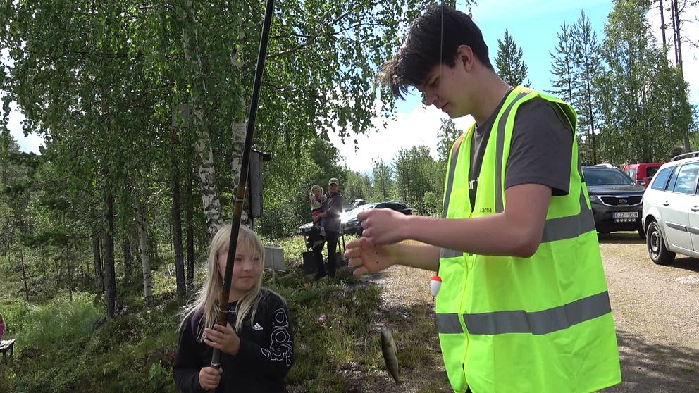 Ung flicka med metspö får hjälp att kroka av liten abborre