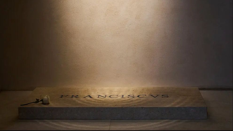 Enkel bild. En belyst gravsten med texten ”Franciscus” mot en enkel, ljus bakgrund.