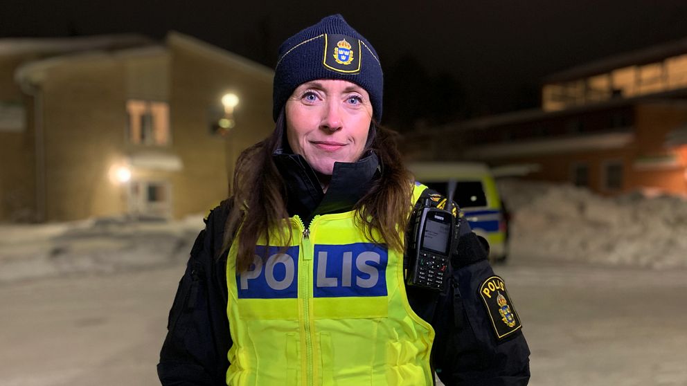 En polis utomhus i mörkret med en polisbuss i bakgrunden