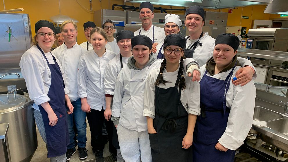 Elever och lärare står i kockkläder i restaurangköket på Ljungbergsgymnasiet i Borlänge.