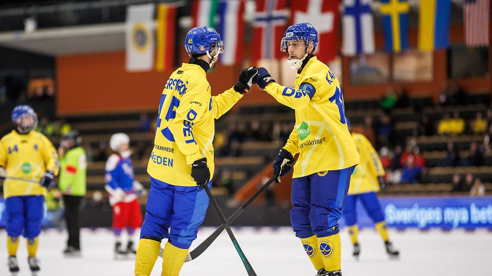 Två svenska bandyspelare i gula tröjor ger varandra en ”high-five” på isen.