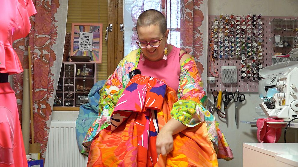 En kvinna sitter med massor av färgglada tyger i famnen