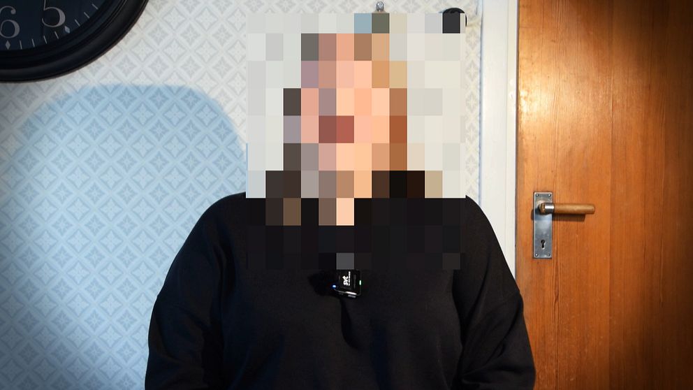 En person med pixlat ansikte framför en dörr och vitmönstrad tapet.