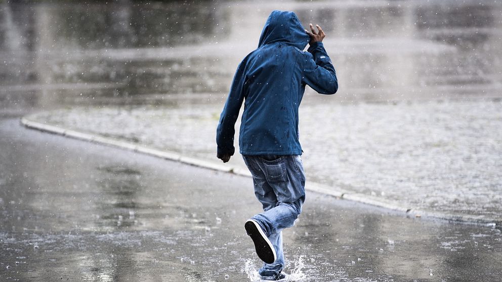 Person i jacka med luva går på gata i regnet.