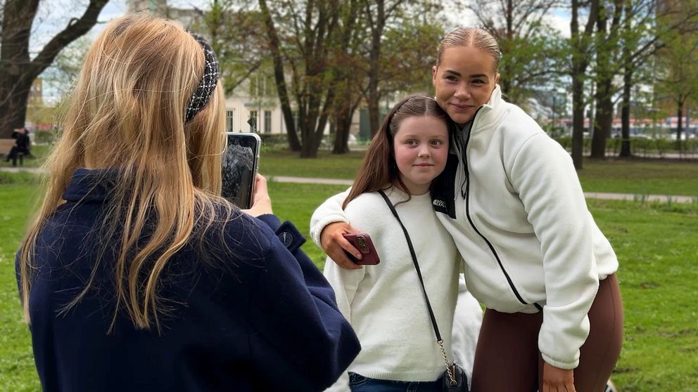 En person fotograferar två personer som poserar tillsammans i en grönskande park.