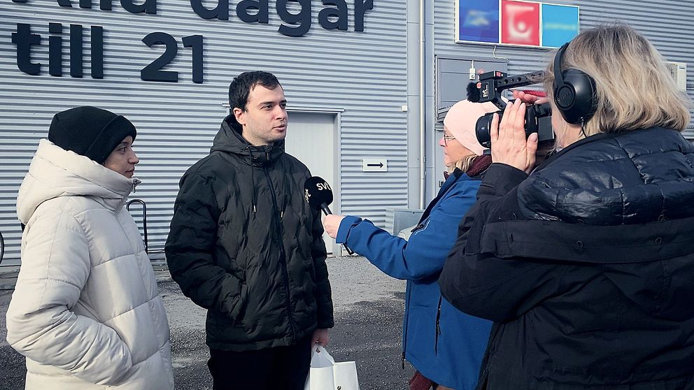 Reporter intervjuar två personer utanför en byggnad.