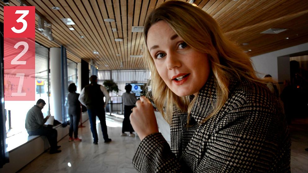 En reporter står i stadshuset, bakom ser man en samling av människor.