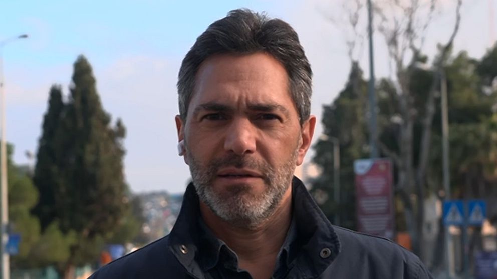 SVT:s Mellanösterkorrespondent Samir Abu Eid står utomhus på en gata med träd och skyltar i bakgrunden under en klar himmel.