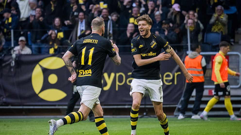 Två AIK-spelare firar mål inför jublande supportrar på fotbollsläktaren.