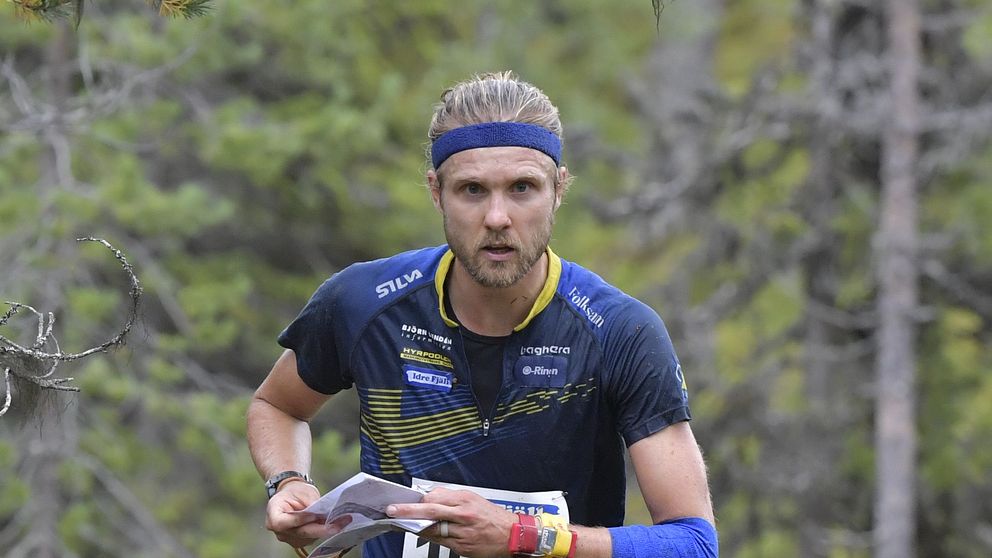 Man springer orientering i skog med karta och nummerlapp.