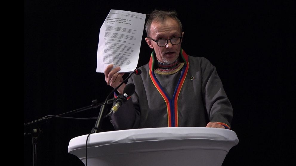 Sametingets styrelseordförande Håkan Jonsson håller upp ett papper från talarstolen på plenum