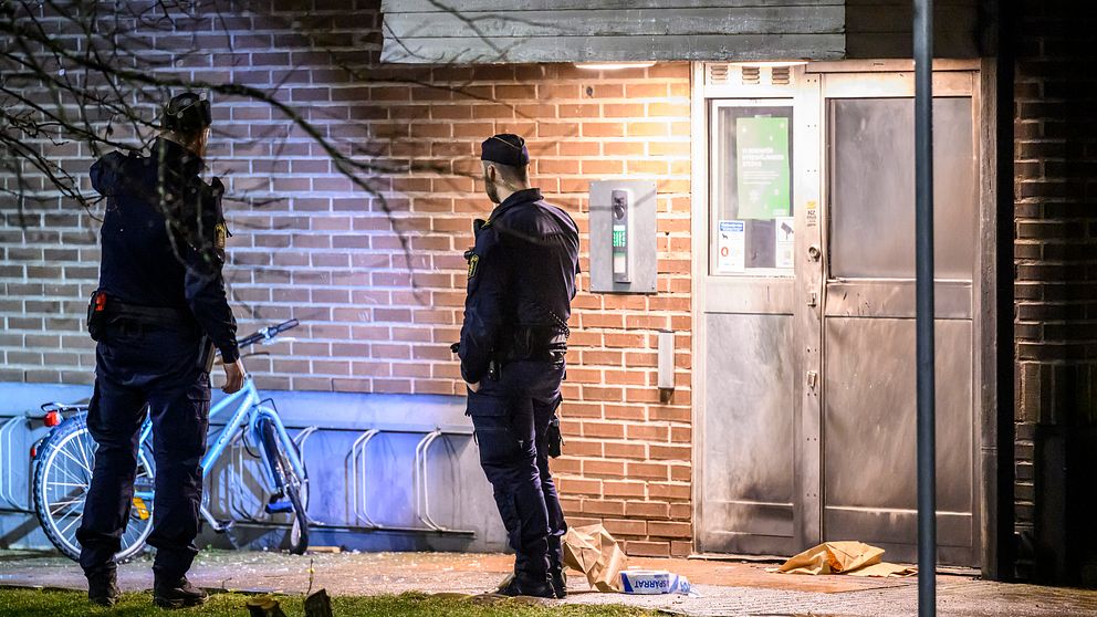 Poliser undersöker en brottsplats vid en tegelbyggnad på natten.