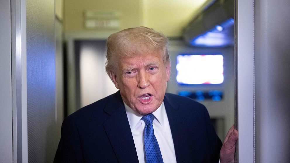 Donald Trump med tv-skärm synlig i bakgrunden.