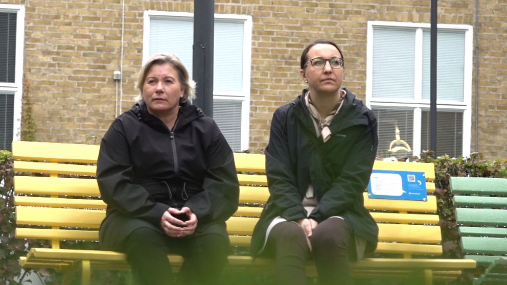 Två kvinnor sitter på en gul bänk.