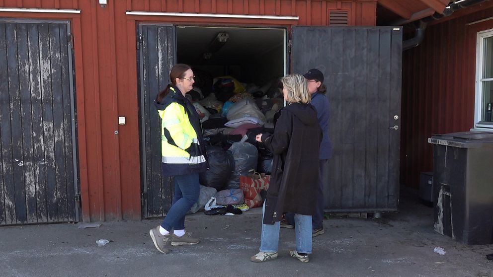 Tre personer står framför ett förråd fyllt med insamlade kläder och saker.