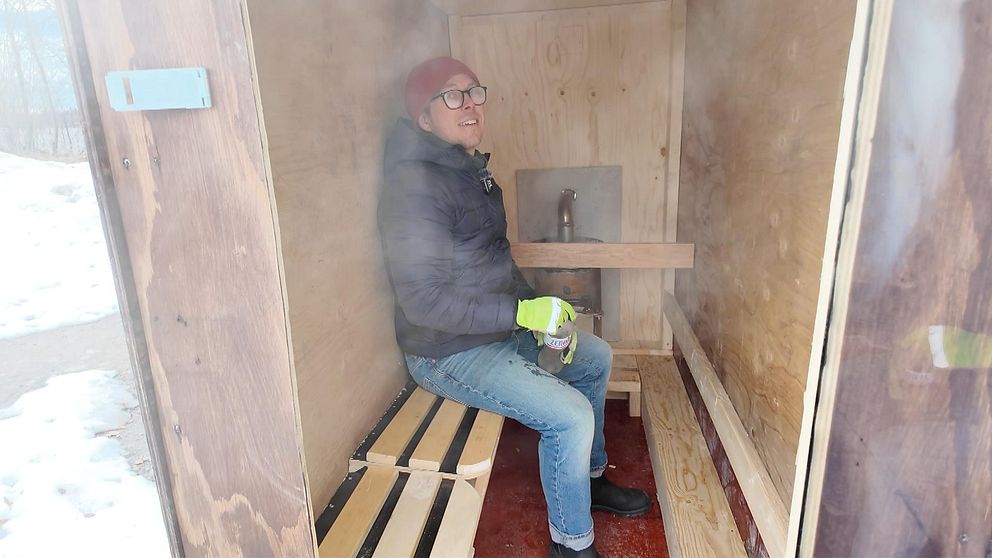 En man sitter i en liten bastu med träinredning och vattenkokare.