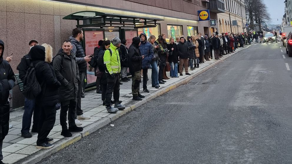 Människor står i en lång kö vid en busshållplats