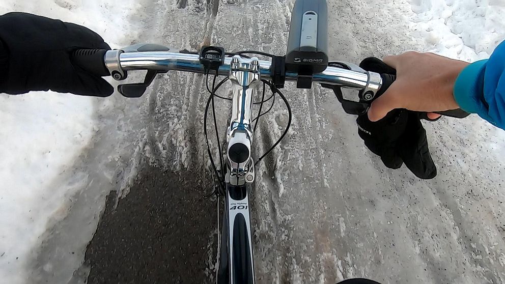 Händer på cykelstyre som färdas på en slaskig cykelväg.