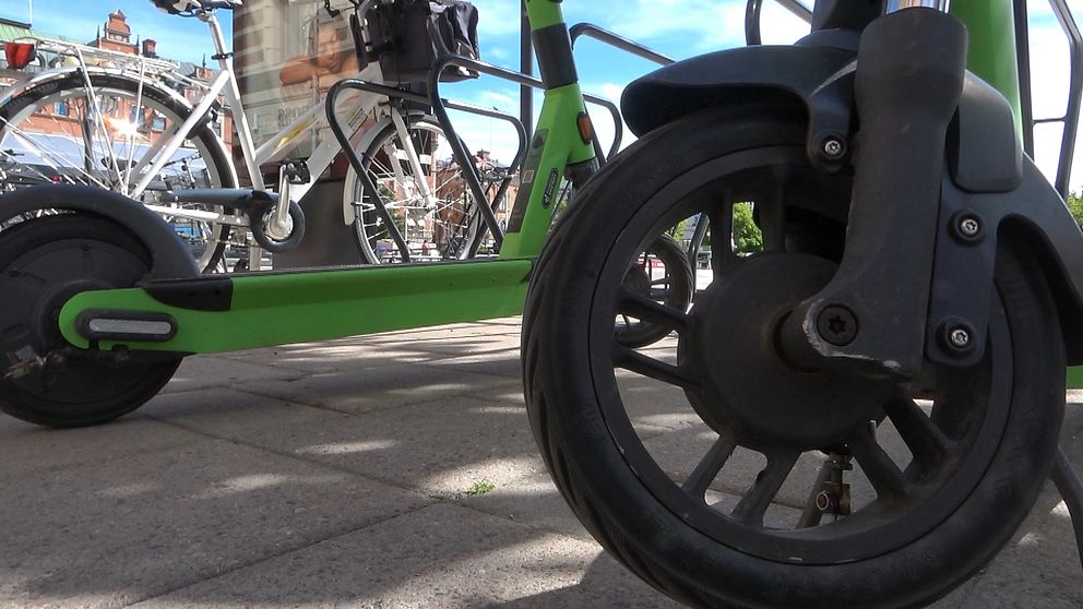 Närbild av elektrisk sparkcykel parkerad bredvid en cykel på trottoar.