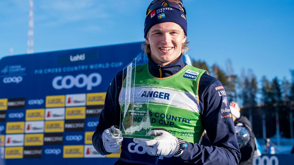 Skidåkare med pokal framför Coop World Cup-skylt. Klarblå himmel i bakgrunden.