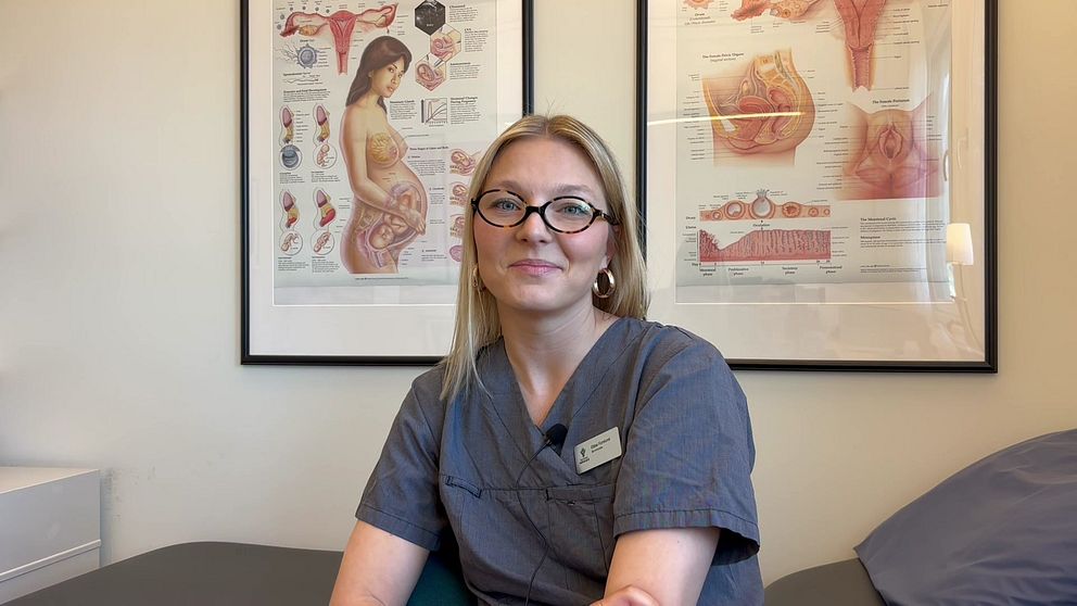 Person i medicinsk uniform framför anatomiska planscher.